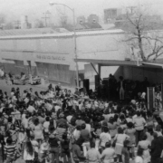 A crowd gathers at a covered stage to hear music during the Cinco de Mayo festival hosted by the West Side Coalition on Santa Fe Drive in the Lincoln Park neighborhood,  Denver, Colorado.  Shows musicians and a large crowd that includes Mexican Americans.
