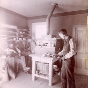Assayers work in a lab probably in Colorado. A stove, mortars, pestles, tongs, and other equipment are in the room.