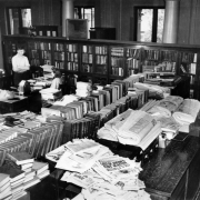 View of the Western History department in the Denver Public Library at Colfax Avenue and Bannock Street in the Civic Center neighborhood of Denver, Colorado. A man and woman stand and sit near a desk. Books and newspapers are in the room.