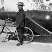 A man stands in profile and holds a bike next to the Rifled Parrot a Civil War cannon in City Park, Denver, Colorado.