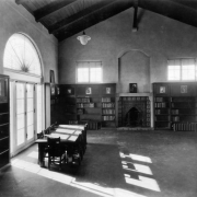 Interior view of the Elyria branch of the Denver Public Library in the Elyria-Swansea neighborhood of Denver, Colorado; decor includes open-beamed ceilings, a fireplace, book shelves, hanging lamps, French and lunette windows.