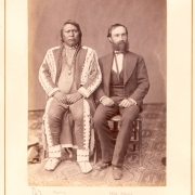 Sitting studio portrait of Native American (Tabeguache band, Southern Ute) Chief Ouray, and Otto Mears, an interpreter and businessman. Ouray wears beaded moccasins, leggings, shirt, and fringed coat, Mears wears a three piece suit.