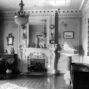 Interior view of the Alonzo Thompson residence (Baerresen Brothers Architects) in Denver, Colorado; the drawing room has French Empire style decor which includes classical entablature, leaded glass, dentils, plaster ornament, a chandelier, a sculpture, a fireplace, torcheres, mirrors, and urns.