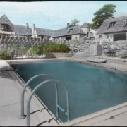 View at Charlford, near Sedalia, Douglas County, Colorado; a manor designed in 1926 for Charles Johnson by Burnham and Merrill Hoyt and built of native volcanic rock. A canvas sun shade and folding chairs are by the swimming pool; the house has a bay window and tower.
