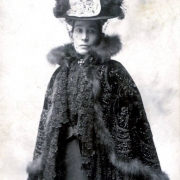 Hispanic American Damiana Rivera de Barela, wife of Colorado State Senator Casimiro Barela, poses for a portrait in an embroidered cape trimmed in fur and a hat decorated with feathers, a bow and a veil.  She wears a pin in the shape of a cross.