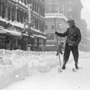 A man skis in a downtown Denver street in the snowstorm of 1913 in Colorado. Shows pedestrians in the snow packed street.