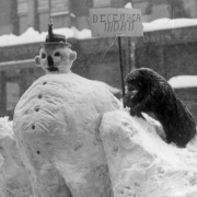 View of a stuffed animal posed beside a snowman with a hat on in the snowstorm of 1913 in Denver, Colorado. A sign reads, "December Morn."