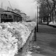View of snow piles on street after the snowstorm of 1913 in Denver, Colorado. Shows a Denver Tramway trolley car number "307" and hitching posts. A sign on a building reads, "Drug Store."