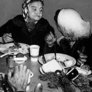 Two women eat Christmas dinner at the Citizen's Mission at 1617 Larimer Street in Denver, Colorado. Shows a Christmas table decoration of pine bough and colored bulbs. The women wear scarves and winter coats.