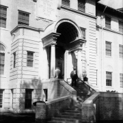 A man with a beard and a cane stands on the steps of the J.K. Mullen Home for the Aged (later the Little Sisters of the Poor Mullen Home) at 3629 West 29th (Twenty-ninth) Avenue in the West Highland neighborhood of Denver, Colorado. Shows a neoclassical style portico and stairs. The carvings above the entryway read: "J.K. Mullen Memorial to the Little Sisters of the Poor" and "Home for the Aged."