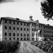 A car sits in front of the dirt driveway of the J.K. Mullen Home for the Aged (later the Little Sisters of the Poor Mullen Home) at 3629 West 29th (Twenty-ninth) Avenue in the West Highland neighborhood of Denver, Colorado. Shows a four story neoclassical building with cupola and portico.