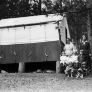 Women and children from the Neighborhood House Association stand and sit on chairs near a tent at a summer camp at Glenisle (Park County), Colorado. Shows a canvas tent with metal sides. Sign on the tent reads: "Dixie."