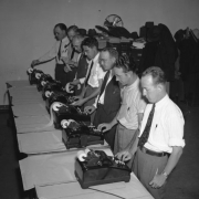 Men identified as Rocky Mountain News staff members stand in a row in front of tables that hold election tabulating machines inside the Rocky Mountain News building at 1720 Welton Street in Denver, Colorado. Some men work the machines, others study tapes with results from the machines.