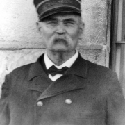 Albert Walters, first Warden at the State Penitentiary in Canon City, Colorado, poses in a double breasted coat, bow tie, and conductor's cap reading: "Cellhouse." He has a "walrus" moustache.