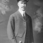 Studio portrait of Casimiro Barela, Colorado state senator for over 37 years. He poses in a suit with a morning coat and wears a top hat,  a tie and stick pin and holds a walking cane with a decorated metal top. He has gray hair and a full, trimmed mustache.