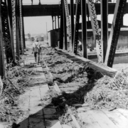 View of Cherry Creek flood damage in Denver, Colorado after the Castlewood Canyon Dam break; shows a railroad bridge, debris, and a man.