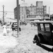 View of Cherry Creek flood damage in Denver, Colorado after the Castlewood Canyon Dam break; shows 16th (Sixteenth) Street, mud, automobiles, storefronts, people, and signs: "Postal Telegraph," "Barteldes Seed Warehouse," "Great Western Stove Co.," and "Salad-Roni."