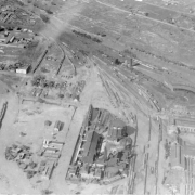 Aerial view of Cherry Creek flood damage in Denver, Colorado after the Castlewood Canyon Dam break; shows railroad yards, the Denver Gas Works, a roundhouse, and the South Platte River.
