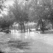 View of Cherry Creek floodwater in Denver, Colorado after the Castlewood Canyon Dam break; shows Speer Boulevard, automobiles, and Sunken Gardens under water.
