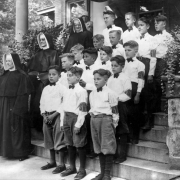 Sisters of Charity and boys from Mount St. Vincent's Home stand on the steps at the home of J. K. Mullen at 896 Pennsylvania Street in the Capitol Hill neighborhood of Denver, Colorado. The boys wear white shirts, bow ties, short pants, and armbands that read: "SVH."
