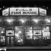 Nighttime view of Pell's Oyster House restaurant at 520 16th (Sixteenth) Street in downtown Denver, Colorado; features leaded glass, gilt letters, garlands, and signs: "Pell's Clams, Pell's Fish House, Pell's Oyster House."
