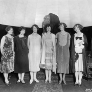 Beauty contestants pose at Lakeside Amusement Park in Lakeside (Jefferson County), Colorado; women's outfits include velvet, fur, lace, and marcel hair styles. A carved wood ottoman and Buddha are in the background.