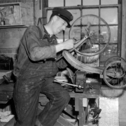 Fireman George R. Schaeffer works on a tricycle in Denver, Colorado; a vise and lunch box are on the work bench.