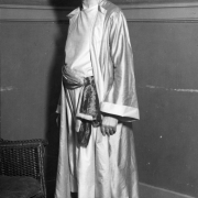 A man poses in costume for a Denver Press Club ball in Denver, Colorado. His outfit has a Moorish motif with robes, embroidery, a turban, and a goatee.