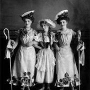 Women pose in Denver, Colorado in Little Bo Peep costume including flowers, lace dresses, grapes, hats, wooden shoes, braids, and shepherds' crooks.