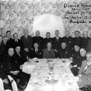 Firemen pose with dinnerware at Joe (Awful) Coffee's Ringside Lounge in Denver, Colorado. The room has floral wallpaper.