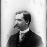 Horace S. Poles poses for a studio bust portrait. The profile portrait shows Poley with a moustache, a starched, upright collar, a tie with a pin, and a jacket.