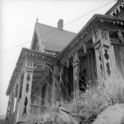 View of the north side of the Lace House, Black Hawk, Colorado. Shows the intricate, modified egg and dart woodwork along the porch frieze;  other jigsaw design at the porch posts and along the bargeboard lining the eaves; board and batten siding, and finials at the roof corner and apex.