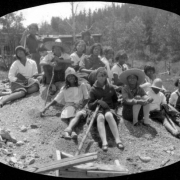 A group of African American teenagers at Camp Nizhoni in Lincoln Hills (Gilpin County), Colorado pose atop a tailings pile near either a silver, gold or tungsten mine. They wear dresses, pants, overalls, stockings, hats. Two have on sombreros, one wears a pith helmet.