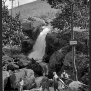 Four African American teenage girls stand at the foot of Alberta Falls (Larimer County), Colorado. They wear overalls or pants, sweaters and boots. A sign on a tree reads: "Alberta Falls."