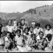 A group of African American female campers, who include Zipporah Parks, pose together on the grounds of Camp Nizhoni in Lincoln Hills (Gilpin County), Colorado. Their counselors (including Marie Anderson, later Marie L. Greenwood) are in the background.
