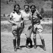 Three African American teenage girls pose together at Camp Nizhoni in Lincoln Hills (Gilpin County), Colorado. They wear jodhpurs with blouses and boots; one wears a tie.