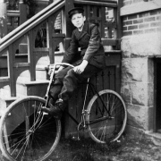 A boy poses on a bicycle by wooden steps in Denver, Colorado; his outfit includes a messenger hat.
