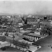 View of Denver, Colorado and snow-capped Front Range mountains. Landmarks include the Pioneer Monument; Arapahoe County Courthouse; YMCA; the Daniels and Fisher tower; and Colfax, Lincoln, and 16th (Sixteenth) Streets. Civic Center landscaping and the roof of the State Capitol are in the foreground.