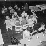 Children eat at tables in a W.P.A. nursery school in Denver, Colorado; food includes cake and tin cups of milk.