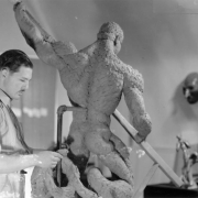 A man works with a clay nude sculpture of a male probably in Colorado.
