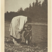 View of a Native American woman and child by the Little Big Horn River probably in Big Horn County, Montana. The mother wears moccasins and a cloth wrap; the child is naked.