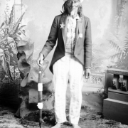 Full length studio portrait of Hairy Chin, Dakota male, dressed in "Uncle Sam" costume, with a top hat and jacket, standing in front of painted backdrop.  Hairy Chin was wearing This costume to lead a Fourth of July parade in Bismarck, North Dakota.