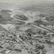Aerial view of a flooded Arkansas River, damaged buildings and rail yards in Pueblo (Pueblo County), Colorado. Shows the Pueblo Smelter, the Nuckolls Packing Company building, standing water identified as "Death Lake", a flooded Missouri Pacific Railway Company rail yard, Denver and Rio Grande Western and Atchison, Topeka and Santa Fe railroad bridges, and City Hall with a domed cupola.