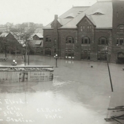 The intersection of B Street and Victoria Avenue is under flood water from the Arkansas River in Pueblo (Pueblo County), Colorado. Shows water in the entrance to the stone Union Depot building, submerged telephone poles and a "St. Louis Refrigerator Car" washed against a drug store building.