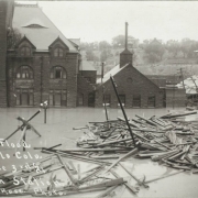 View of lumber and debris near the intersection of B Street and Victoria Avenue in Pueblo (Pueblo County), Colorado. Shows water in the entrance to the stone Union Depot building and submerged telephone poles and trees.