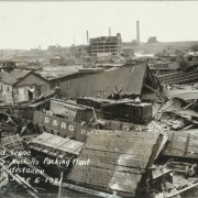 Wrecked buildings and overturned Denver and Rio Grande Western freight cars are in the Walker rail yard after the Arkansas River flood in Pueblo (Pueblo County), Colorado. Shows smokestacks and the Nuckolls Packing Company buildings in the distance.
