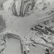 Aerial view of the flooded Arkansas River in Pueblo (Pueblo County), Colorado. Shows freight cars at the washed out Missouri Pacific Railway Company yard, railroad bridges over the river and the Nuckolls Packing Company building beside standing water.