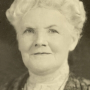 Studio bust portrait of Catherine Smith Mullen (Mrs. John Kernan Mullen) in a lace blouse and dress with a banded collar and a necklace. Mrs. Mullen has short, wavy hair.