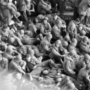 Tenth Mountain Division troops fill the entire frame, except for a small triangle of water in the upper right corner; troops are returning by ship to the U.S.A.  All are in uniform, most wear helmets and some wear life vests. Some are reading, some resting, others look out to sea.