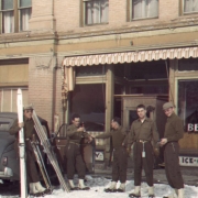 Five Tenth Mountain Division Skitroopers in uniform stand outside a small store at the Jerome Hotel in Aspen, Colorado. Anthony Dillon, far left, holds skis. Man on far right is identified as photographer Bill Southworth.